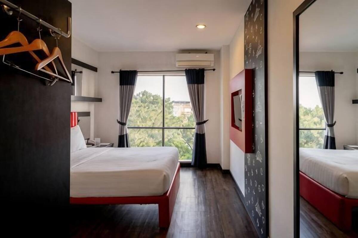 A hotel room with two beds, a large window, and a view of trees.