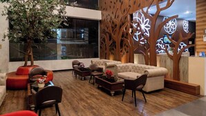 A modern lounge area with a large window, a wooden tree sculpture, and a reception desk. - Kalya Hotel Bandung (Bandung)