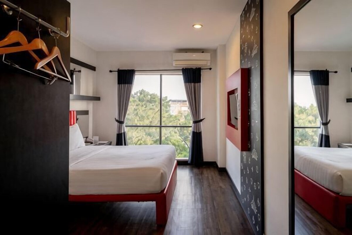 Een hotelkamer met twee bedden, een groot raam en uitzicht op bomen.