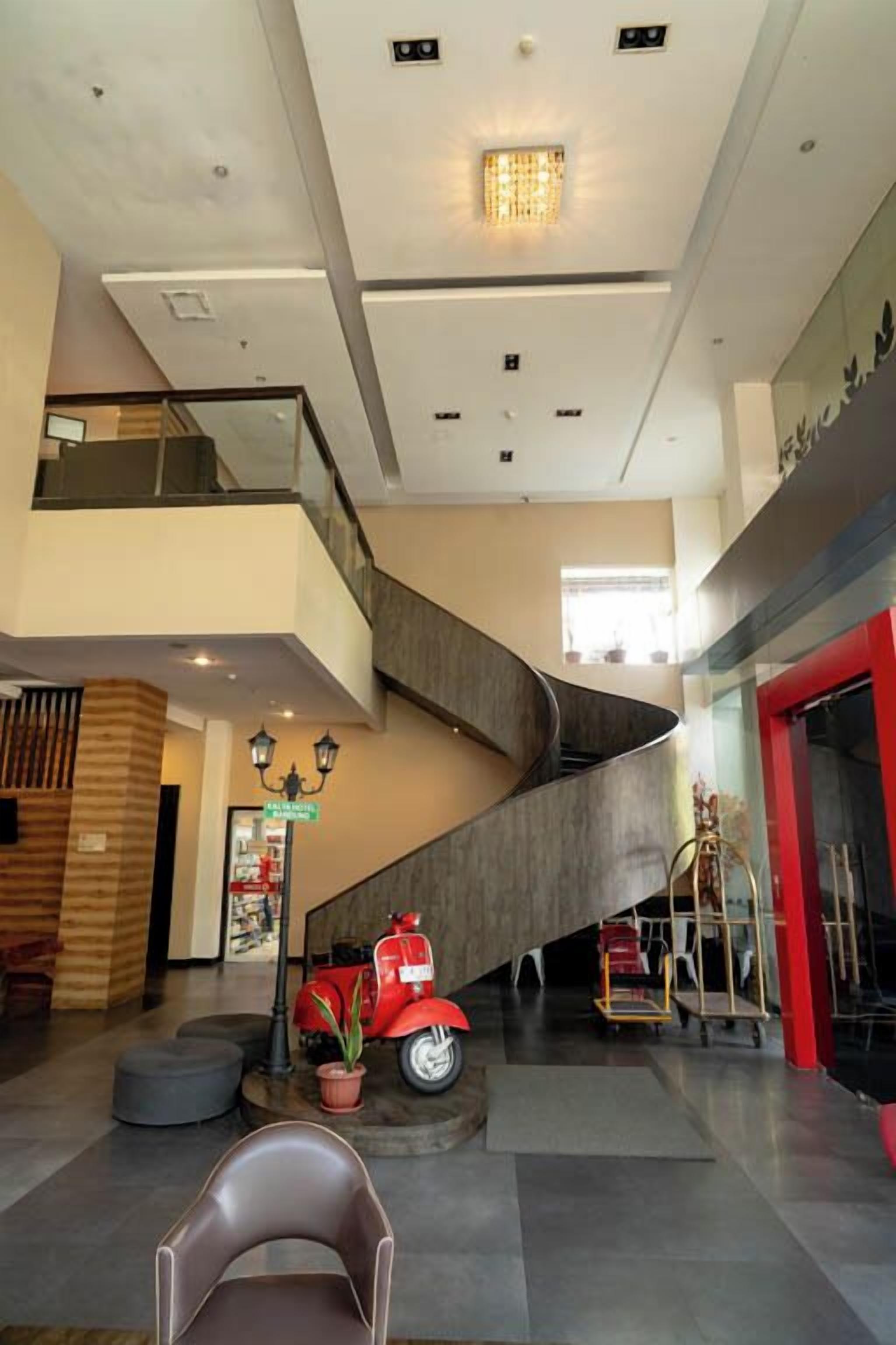 Eine großzügige Lobby mit einer geschwungenen Treppe, einem roten Oldtimer und einem modernen Aufzug.