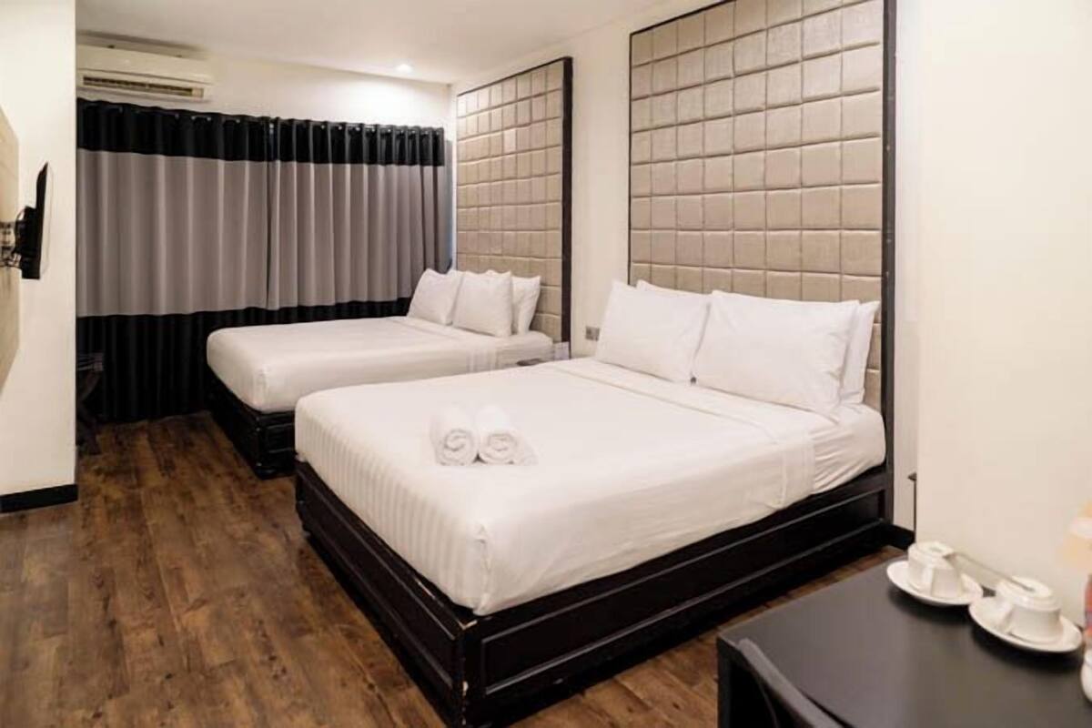 A hotel room with two beds, a wooden floor, a black nightstand, and a curtain.
