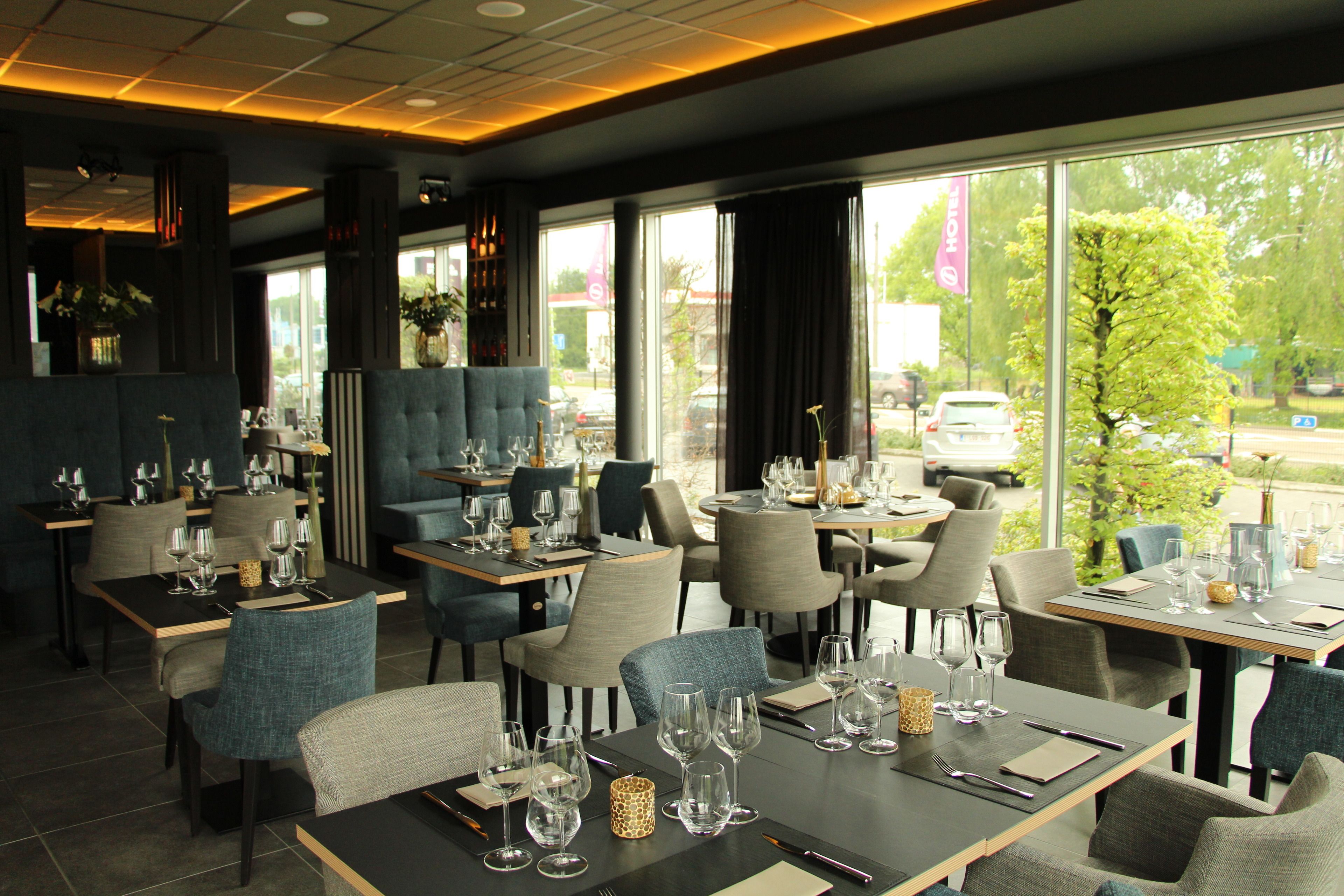 Un restaurant avec des tables dressées pour le service, de grandes fenêtres et une vue sur l’extérieur.