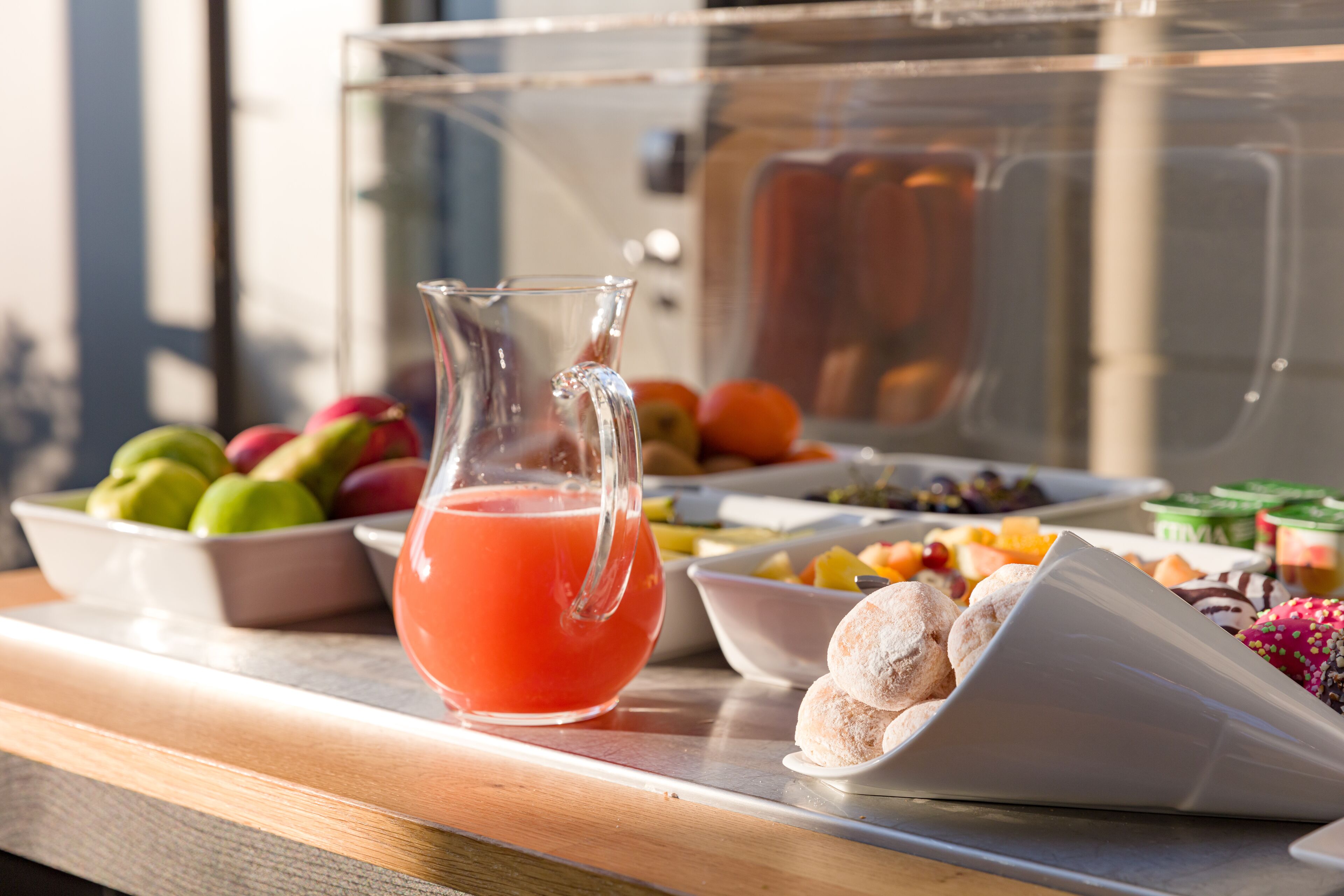 Um buffet de café da manhã com jarra de suco de laranja, potes de frutas e pães.