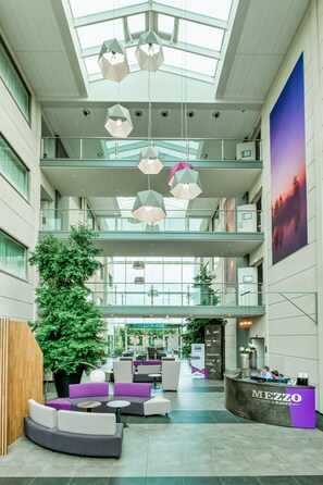 A spacious lobby with a high ceiling, multiple seating areas, and a reception desk. - Mezzo Beringen (Beringen)