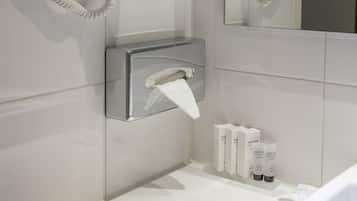A bathroom with a hairdryer mounted on the wall, a towel dispenser, and toiletries on the counter.