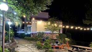 A patio area with string lights, potted plants, and a wooden bench. - Memory In Jeju Pension (Seogwipo)