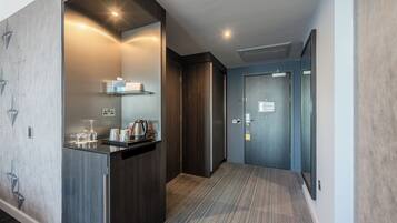 A modern hotel hallway with a built-in kitchenette, a carpeted floor, and a door leading to a room.