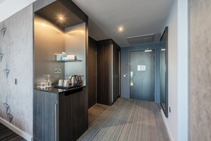 Een moderne hotelgang met een ingebouwde kitchenette, een vloerkleed en een deur naar een kamer.