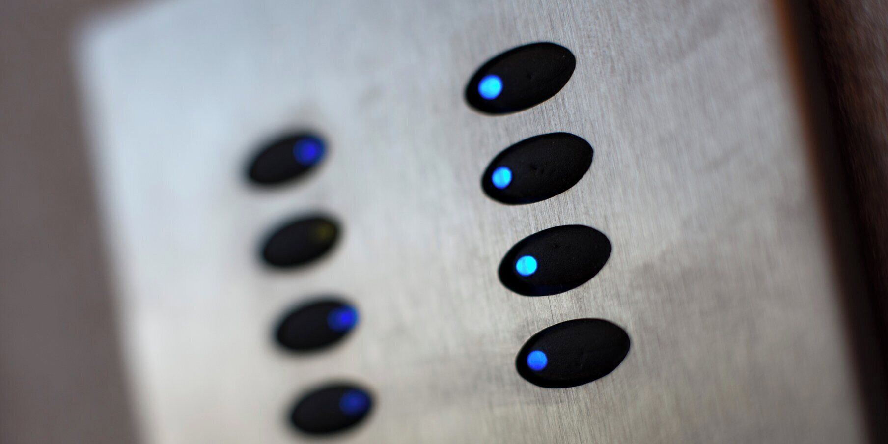 A close-up of a metallic surface with six oval-shaped buttons, each with a blue light indicator.