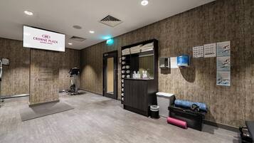 A modern waiting area with a digital sign for Crowne Plaza Aberdeen Airport, a reception desk, a seating area, and informational posters on the wall.