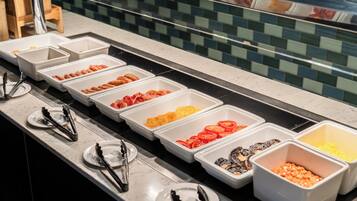 A buffet line with various food items in white trays, including sliced tomatoes, mushrooms, and other vegetables.