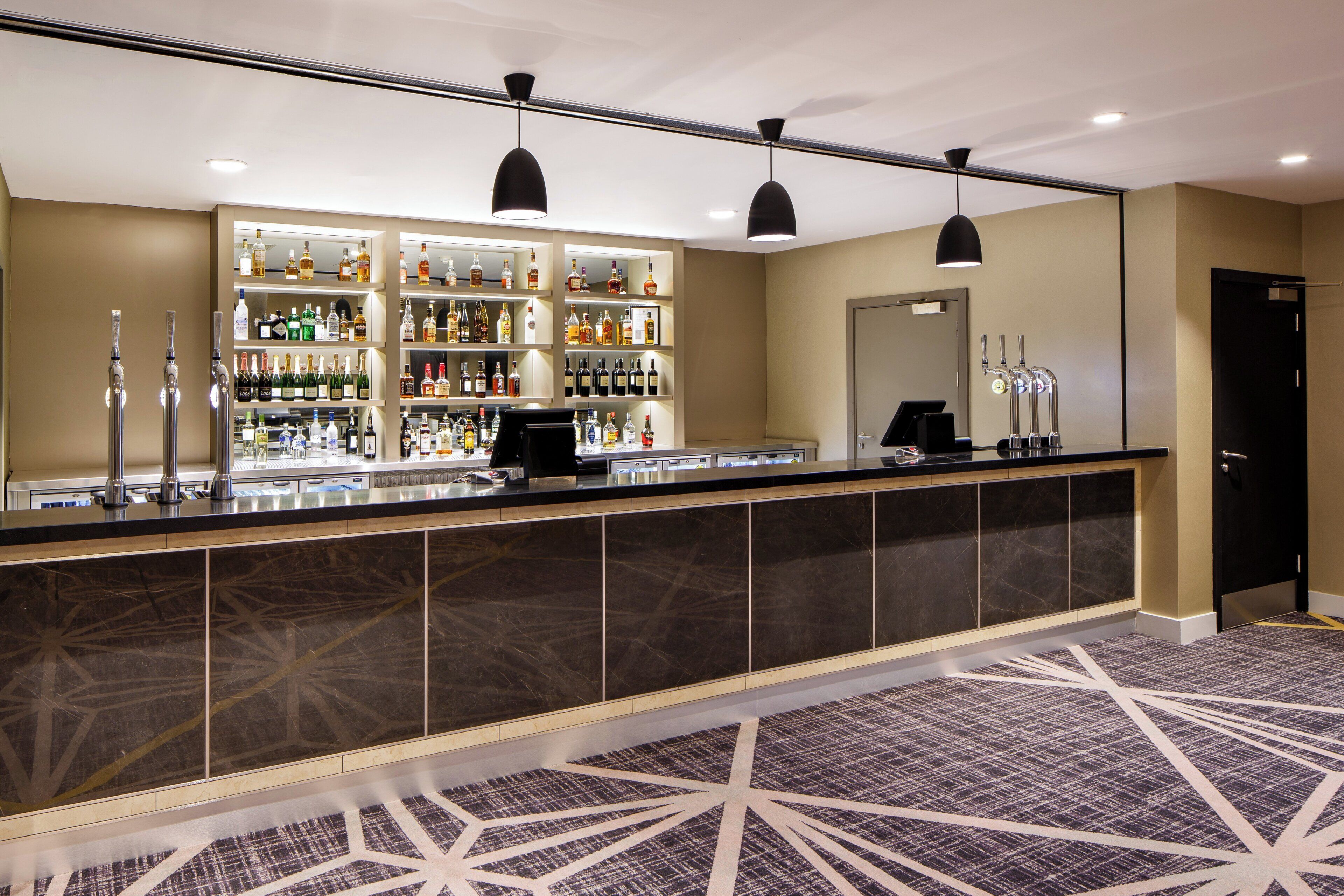 A bar area with shelves of liquor bottles, a cash register, and a black counter.