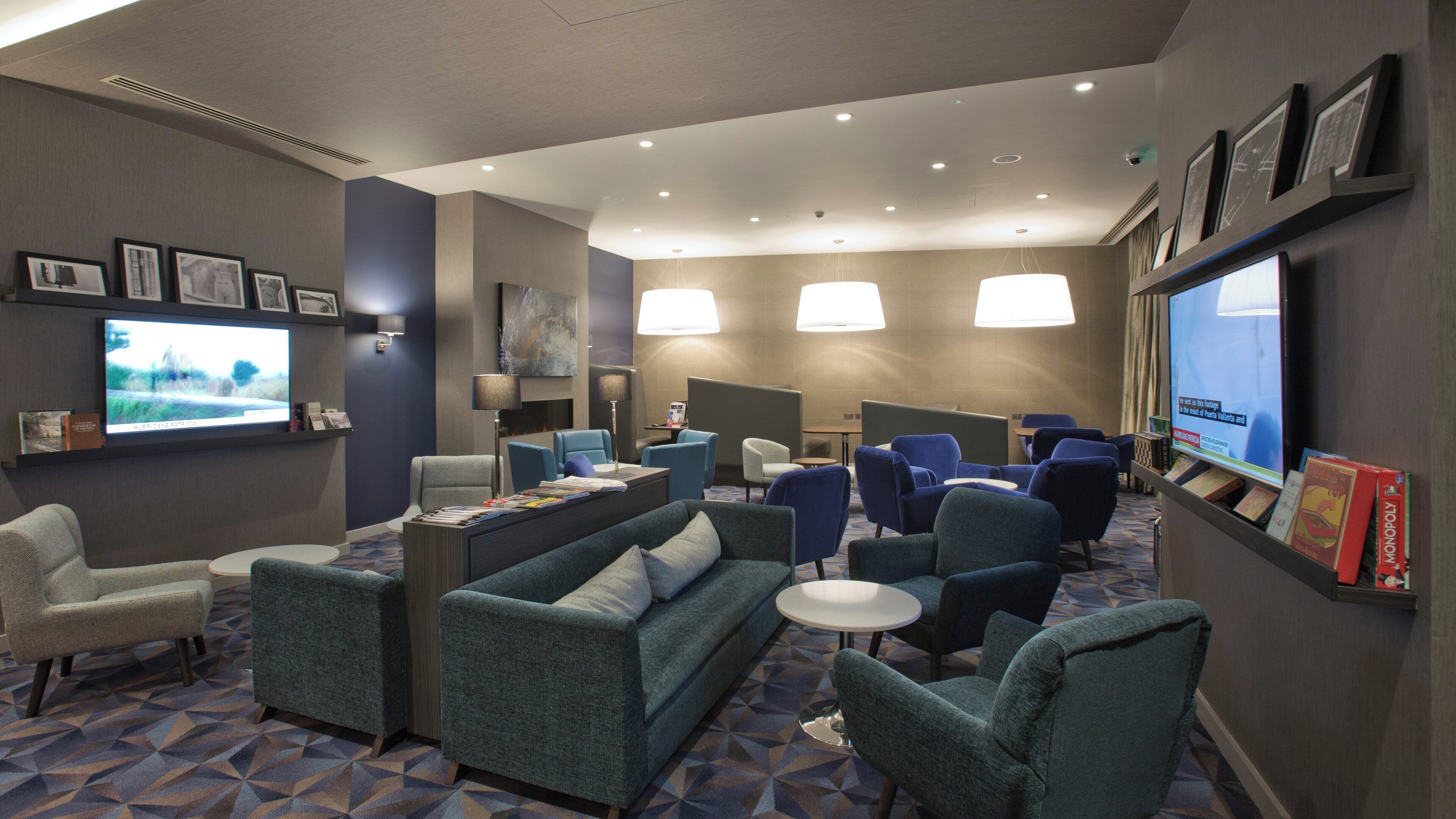 Un hall de hotel con arreglos de asientos, un televisor y una pantalla digital que muestra información.