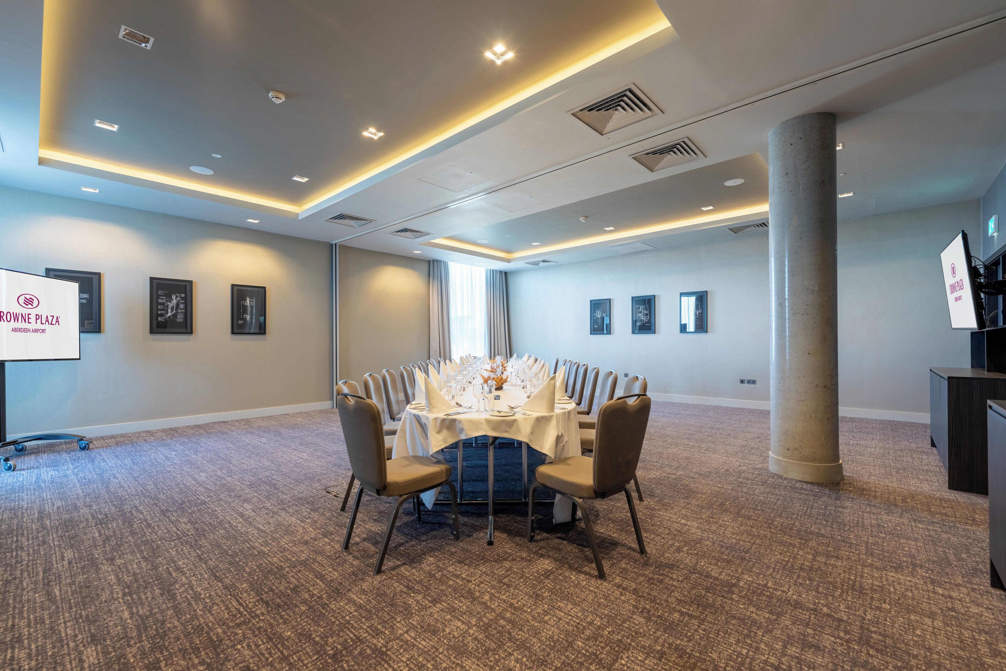 A conference room with a round table, chairs, and a projector screen.