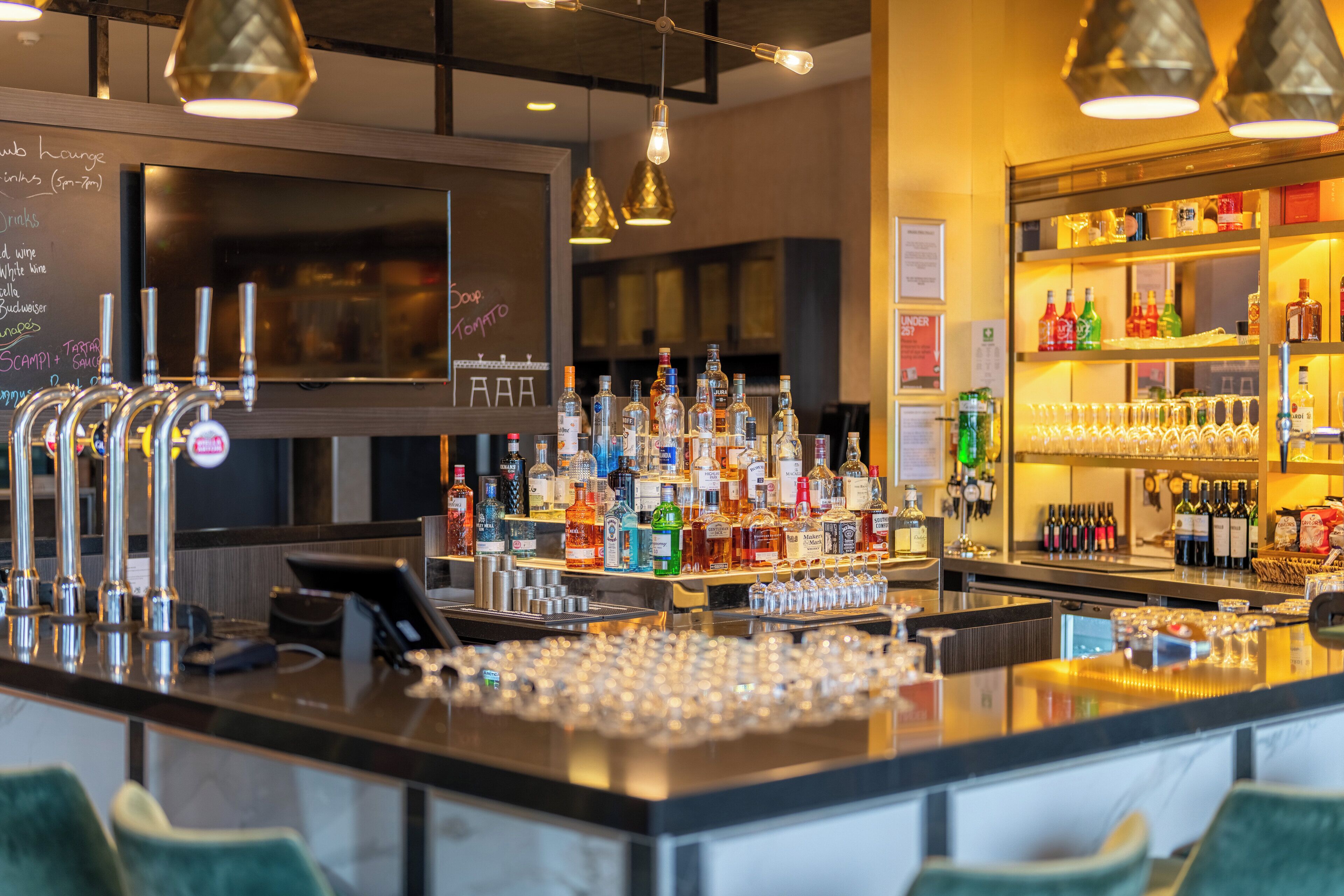 Una zona de bar con múltiples grifos, una variedad de botellas de licor y vasos sobre la barra.