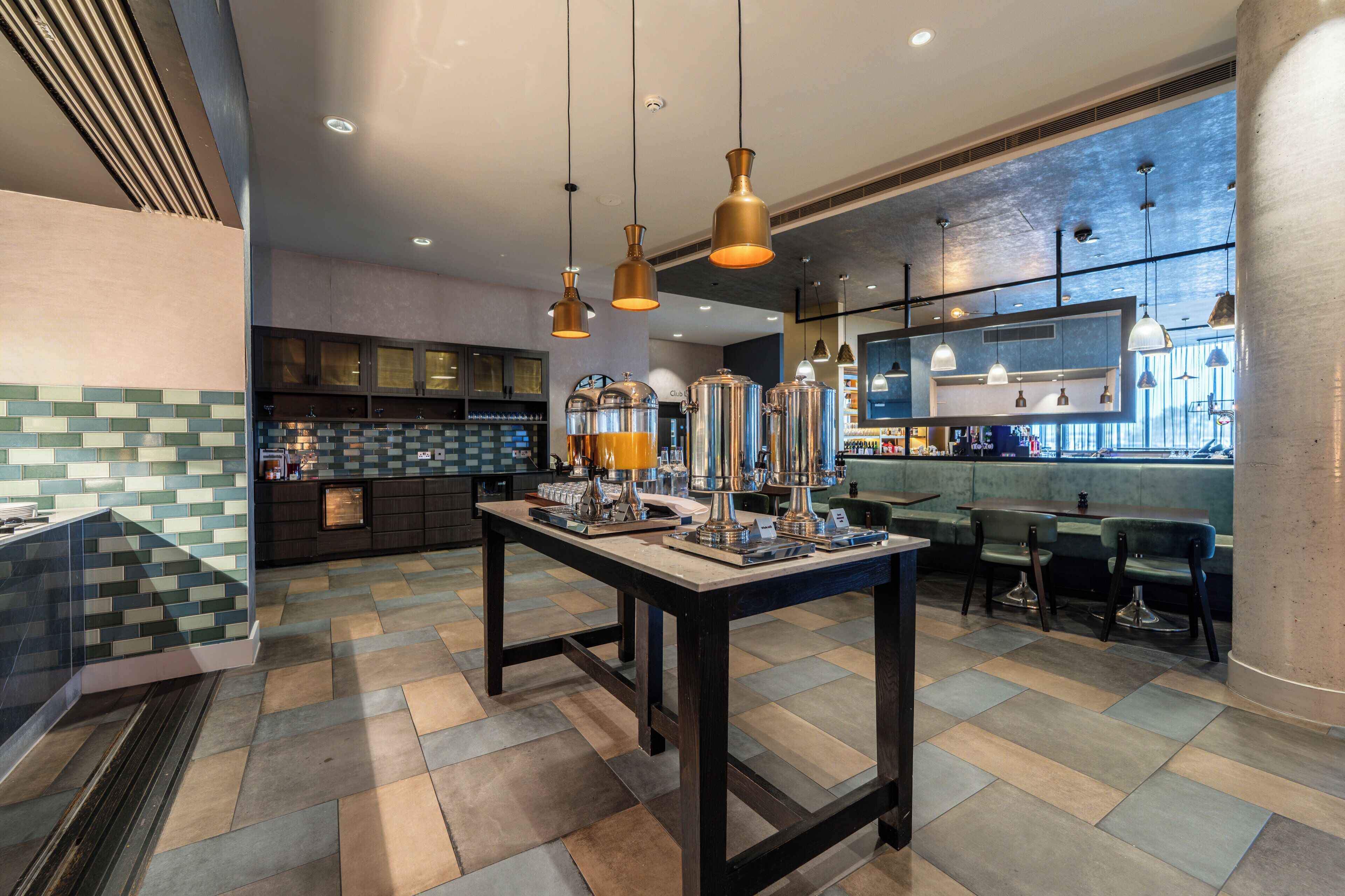 A modern restaurant with a central island, pendant lighting, and a view of the city through large windows.