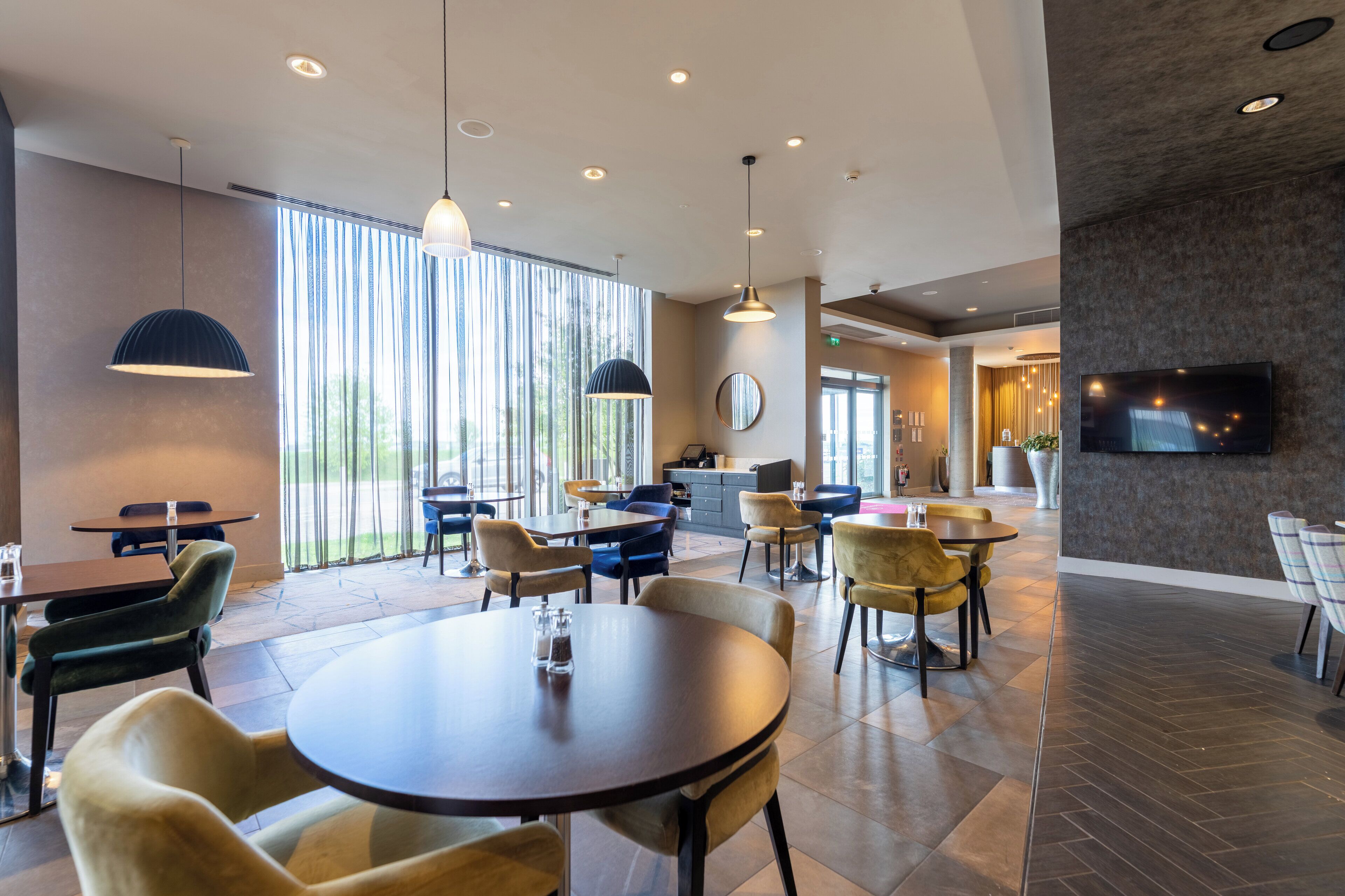 Un espace repas moderne avec des tables et des chaises rondes, de grandes fenêtres et un téléviseur à écran plat fixé au mur.