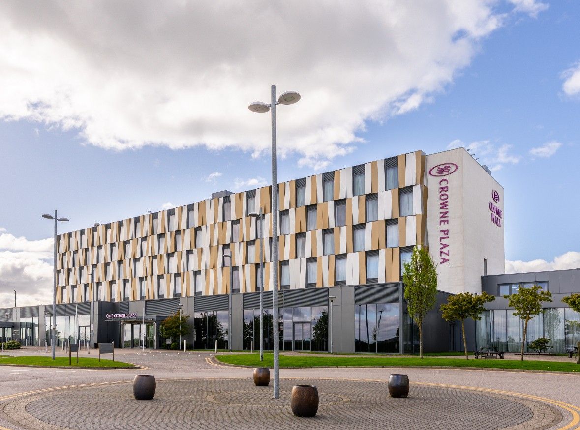 A modern hotel with a distinctive facade, a central entrance, and a circular plaza with seating.