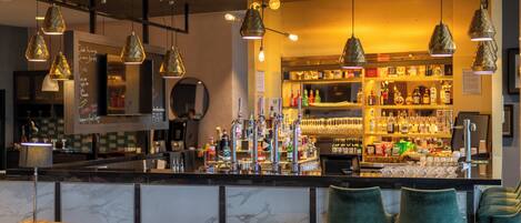 Un espace bar doté d’un comptoir en marbre, de luminaires suspendus et d’un assortiment de bouteilles et de verres.