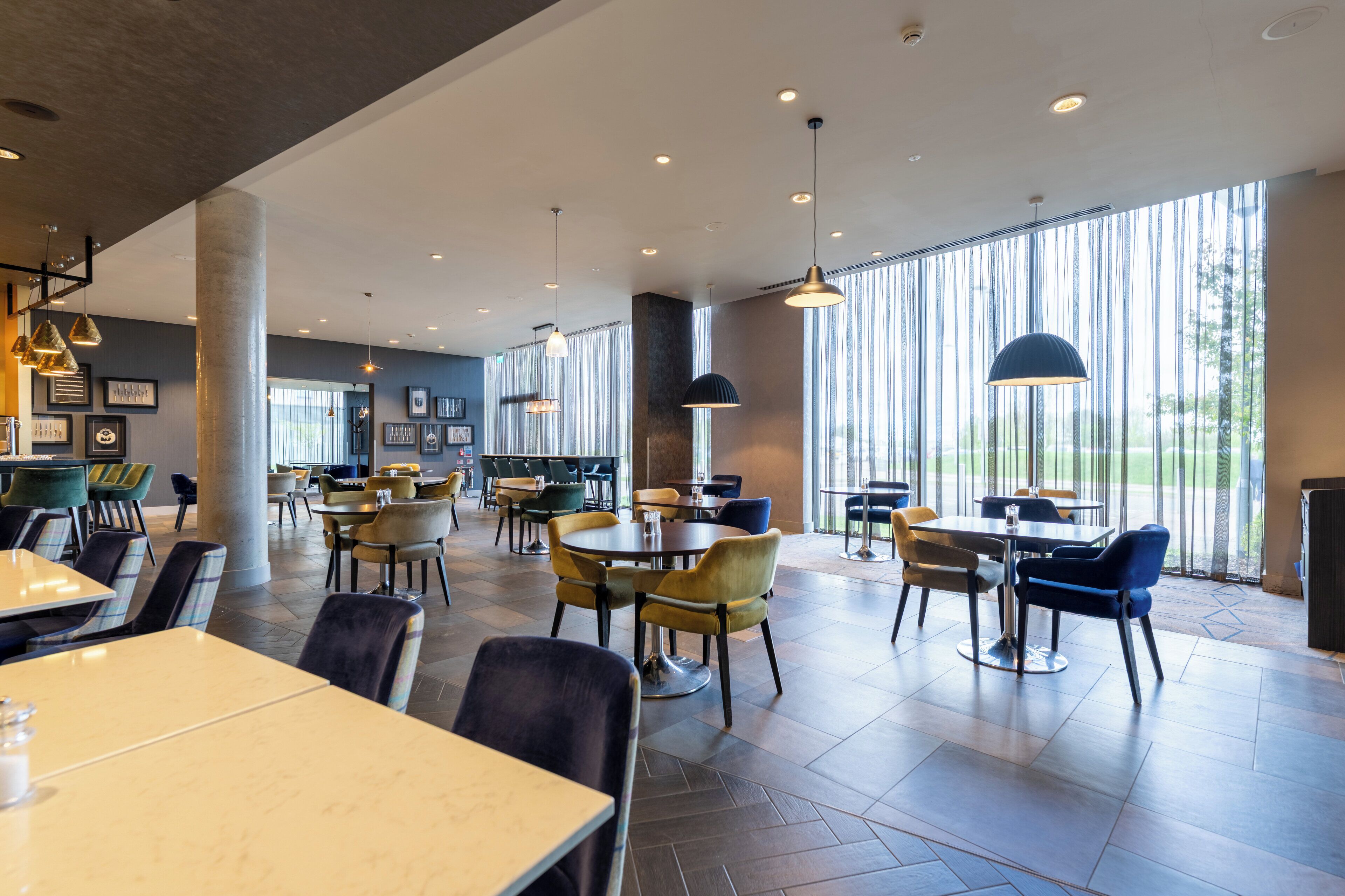 A spacious indoor dining area with multiple tables and chairs, large windows, and pendant lighting.