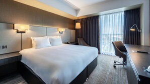A hotel room with a large bed, a desk, and a chair. There are two wall-mounted lamps and a window with curtains. - Crowne Plaza Aberdeen Airport by IHG (Aberdeen)