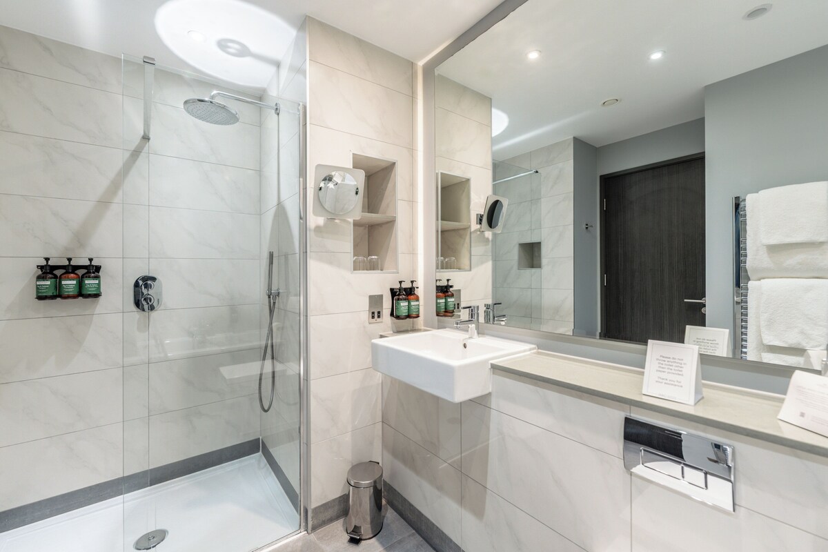 Een moderne badkamer met een douchecabine van glas, een witte wastafel en een grote spiegel.