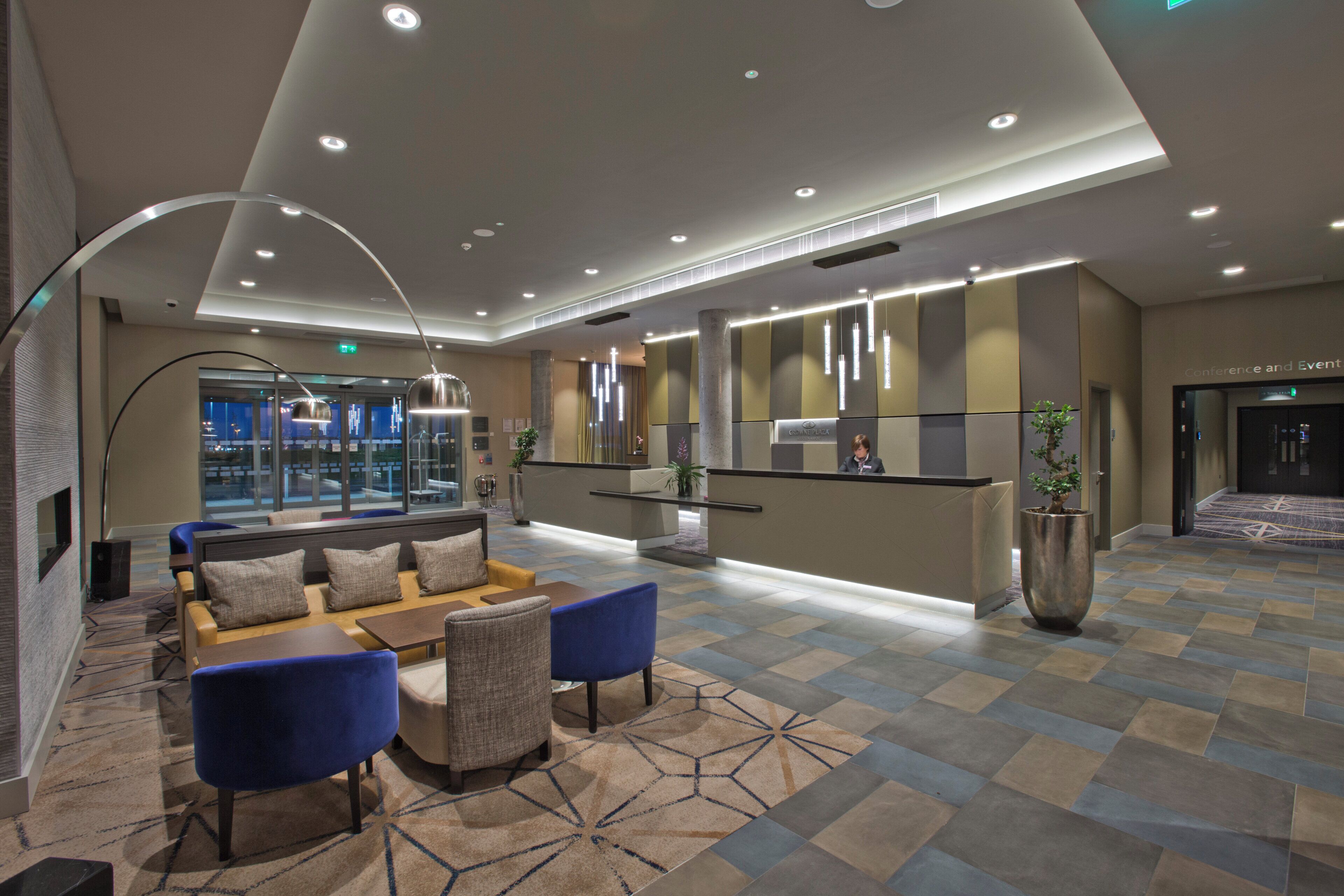 A modern lobby with a reception desk, seating area, and a large potted plant.