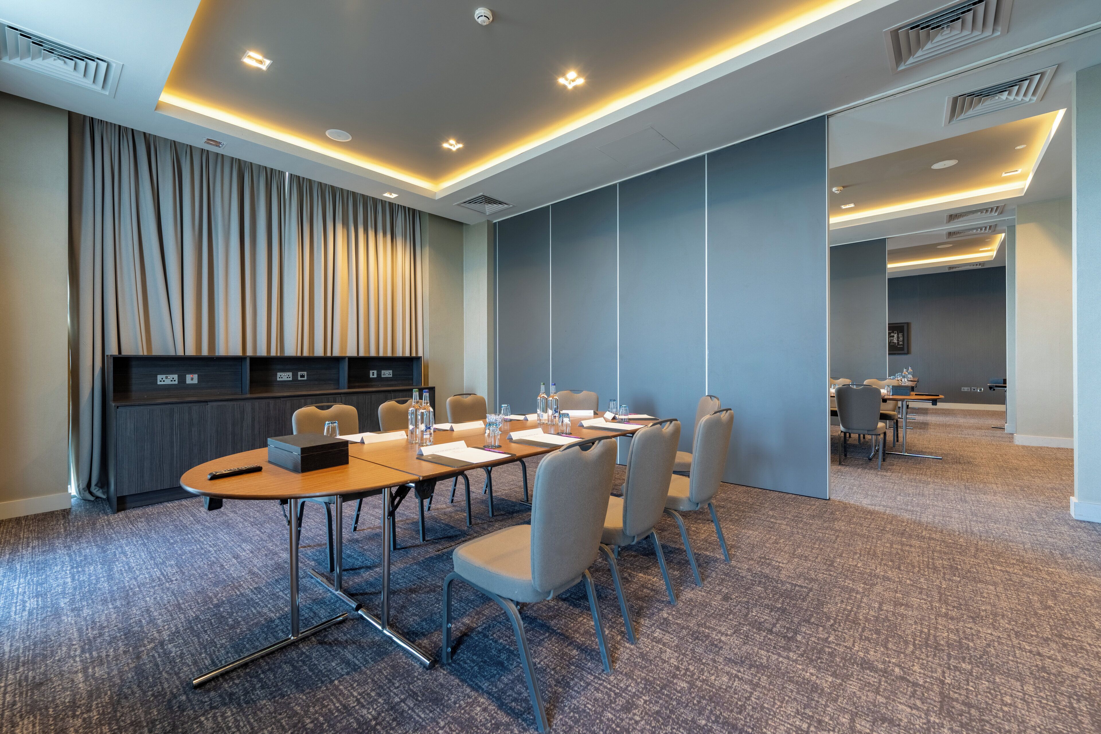 A conference room with a long table, chairs, and a projector screen.