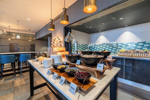 Een ontbijtbuffet met diverse gerechten en een zithoek met blauwe stoelen.