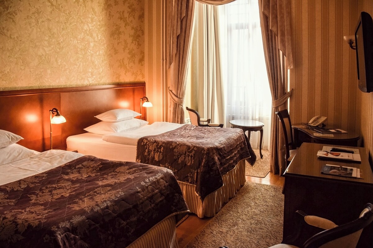 A hotel room with two beds, a desk, a chair, a small table, and a telephone.