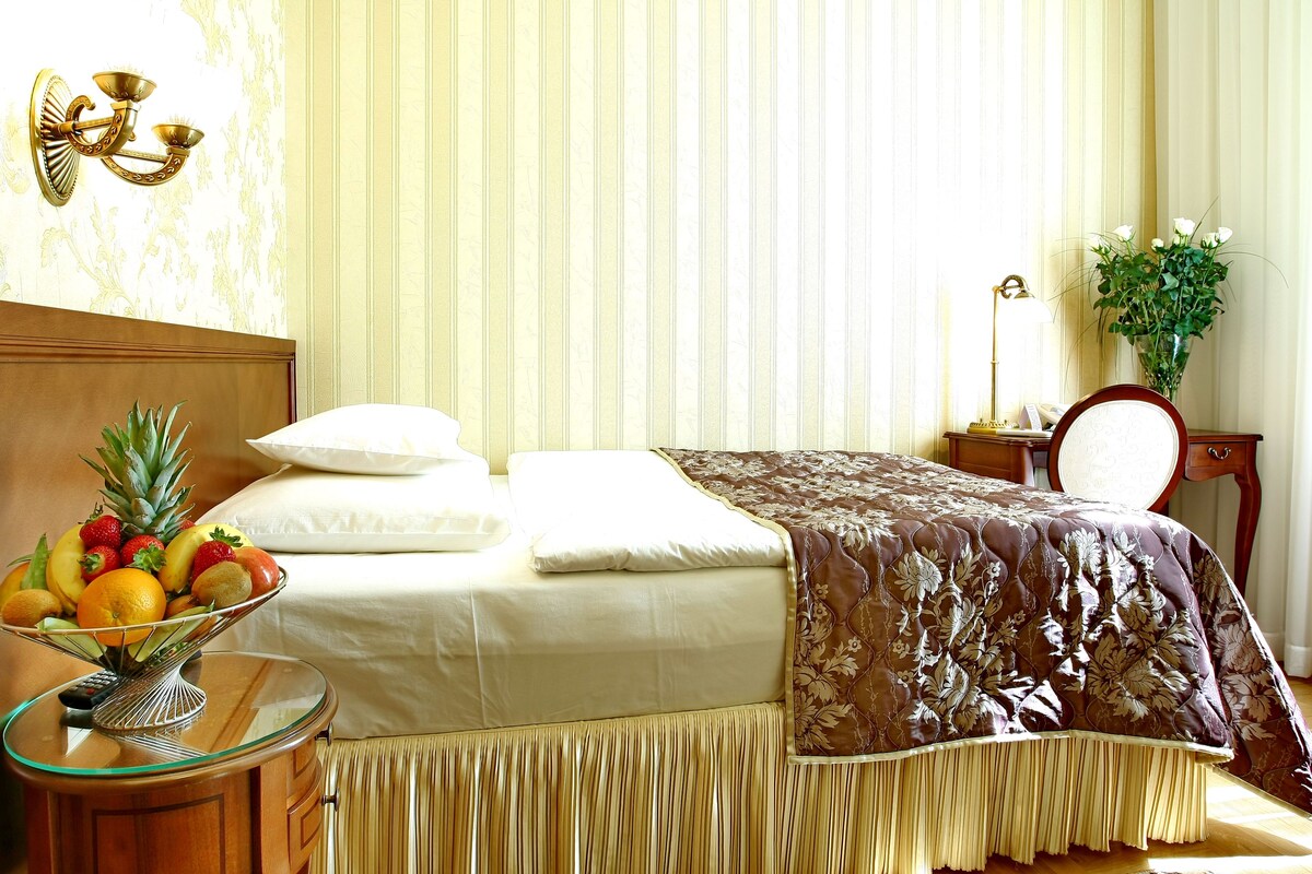 A hotel room with a bed, a bedside table with a fruit bowl, a lamp, and a mirror.