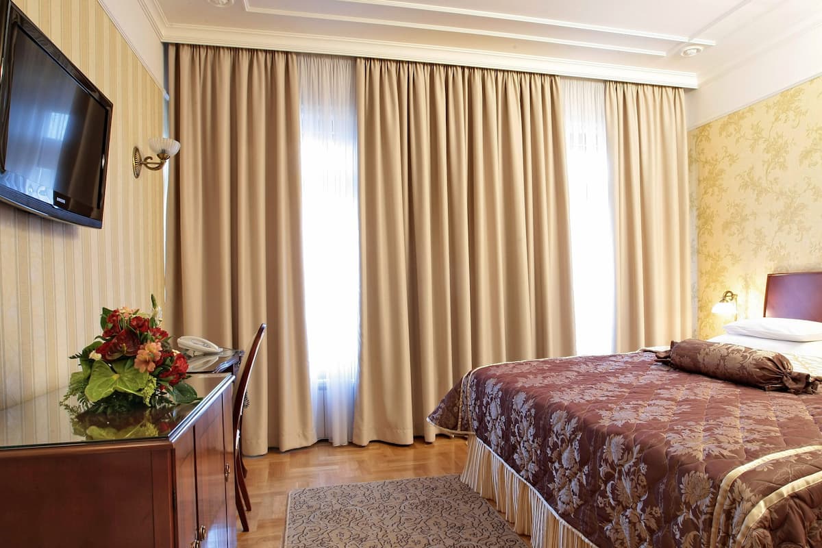 A hotel room with a bed, a desk with a telephone, and a television on the wall.