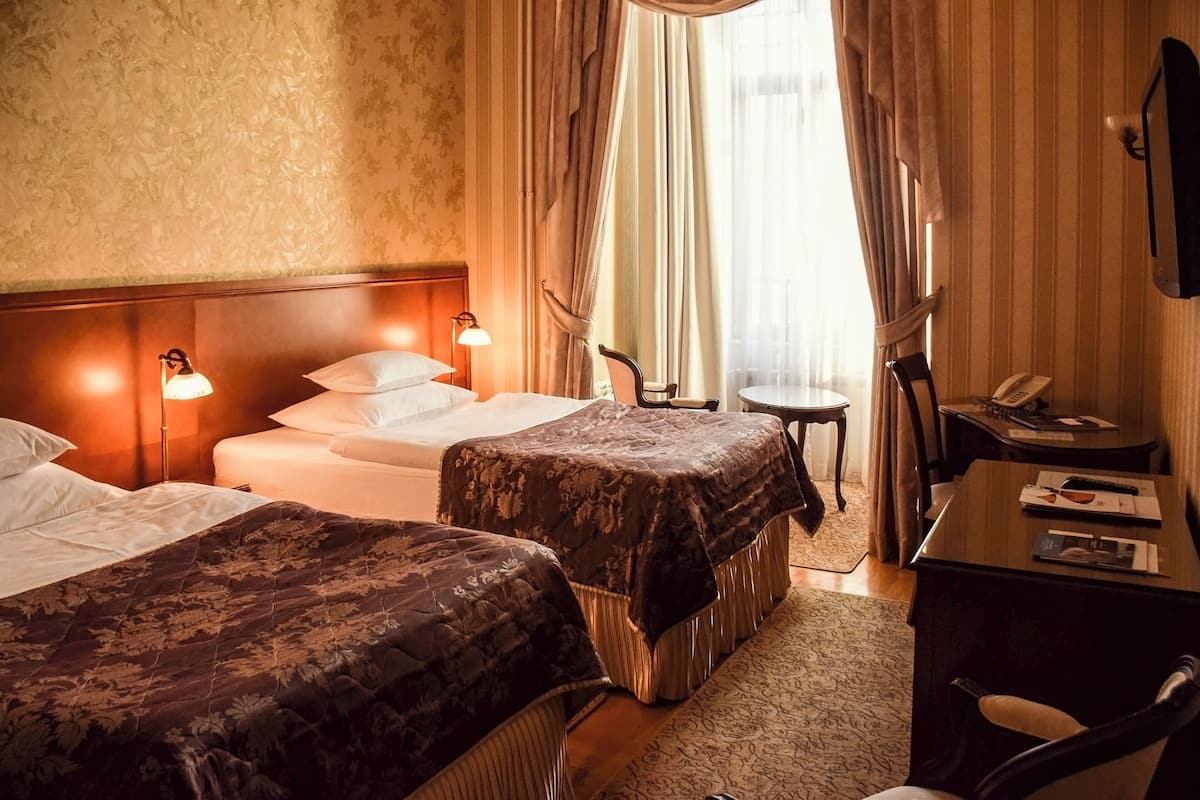 A hotel room with two beds, a desk, a chair, a small table, and a telephone.