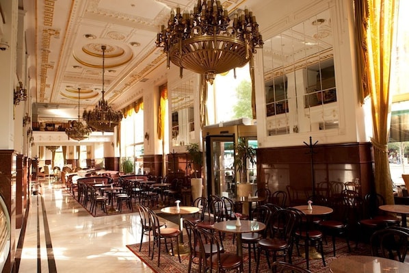 A spacious hotel lobby with multiple seating areas, a grand chandelier, and large windows allowing natural light.