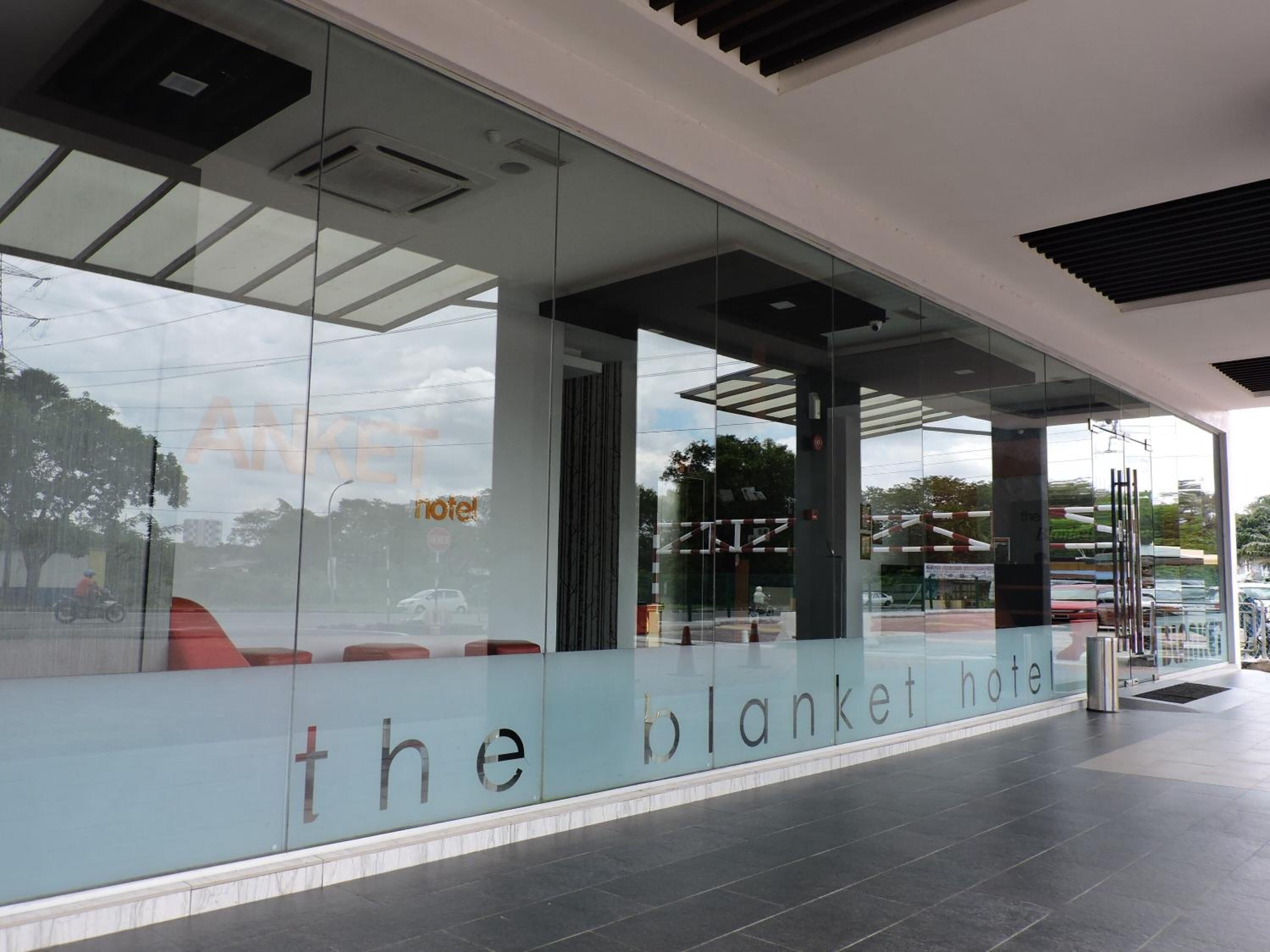 Una entrada de hotel moderna con fachada de vidrio y un letrero que dice "the blanket hotel".