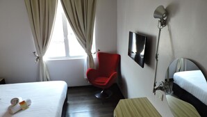 Habitación de hotel con dos camas, una silla roja, un escritorio con espejo y un televisor.
