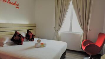 A hotel room with a bed, pillows, a red chair, a window with curtains, and a wall sign.