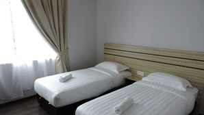 Dos camas individuales con sábanas blancas y toallas enrolladas, un cabecero de madera y una ventana con cortinas.
