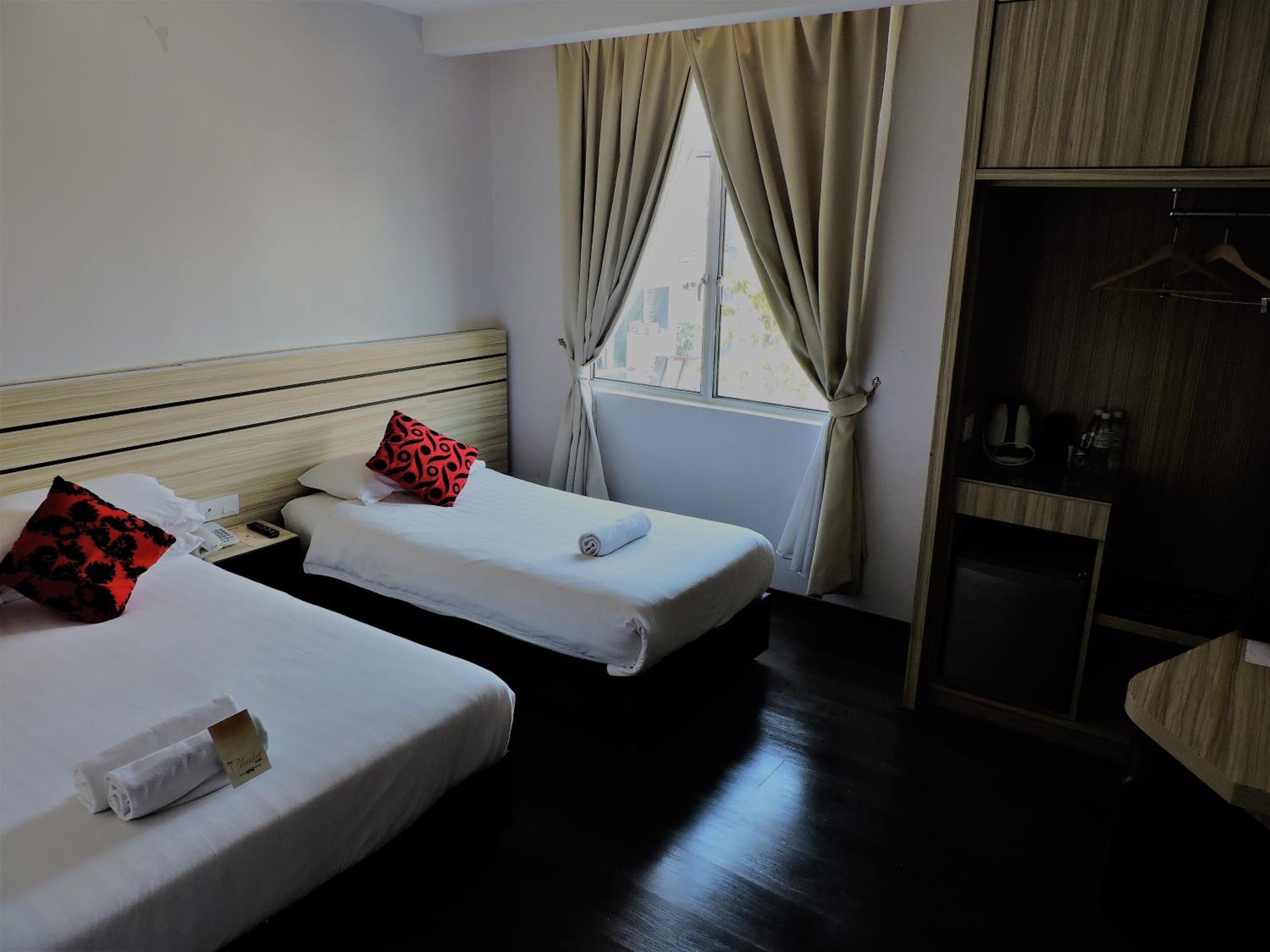 Una habitación de hotel con dos camas individuales, un cabecero de madera, un armario y una ventana con cortinas.