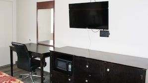 A hotel room with a large desk, a chair, a television mounted on the wall, and a mirror. - Huntington Inn (Huntington)