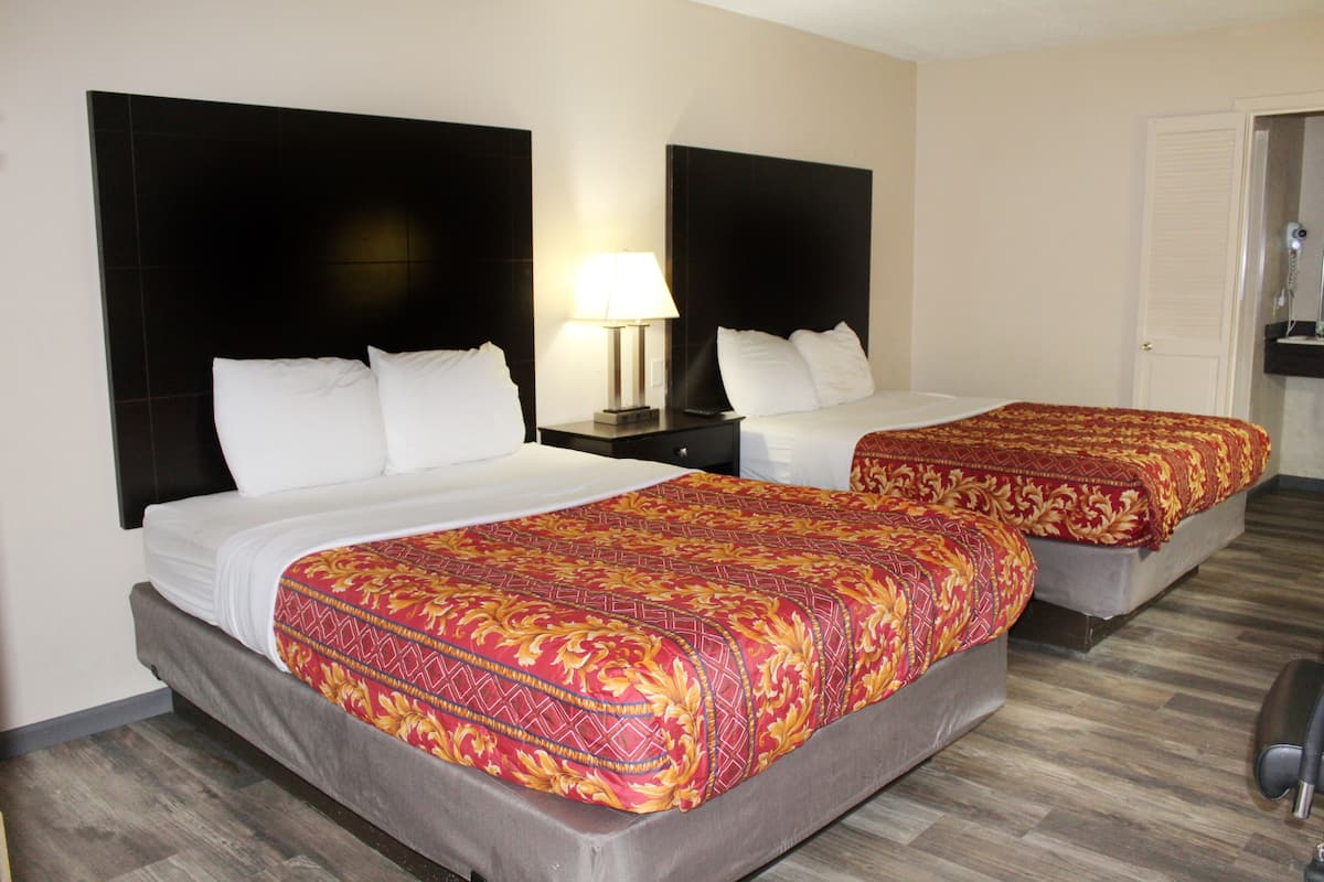A hotel room with two beds, each with a headboard, a nightstand with a lamp, and a wooden floor.