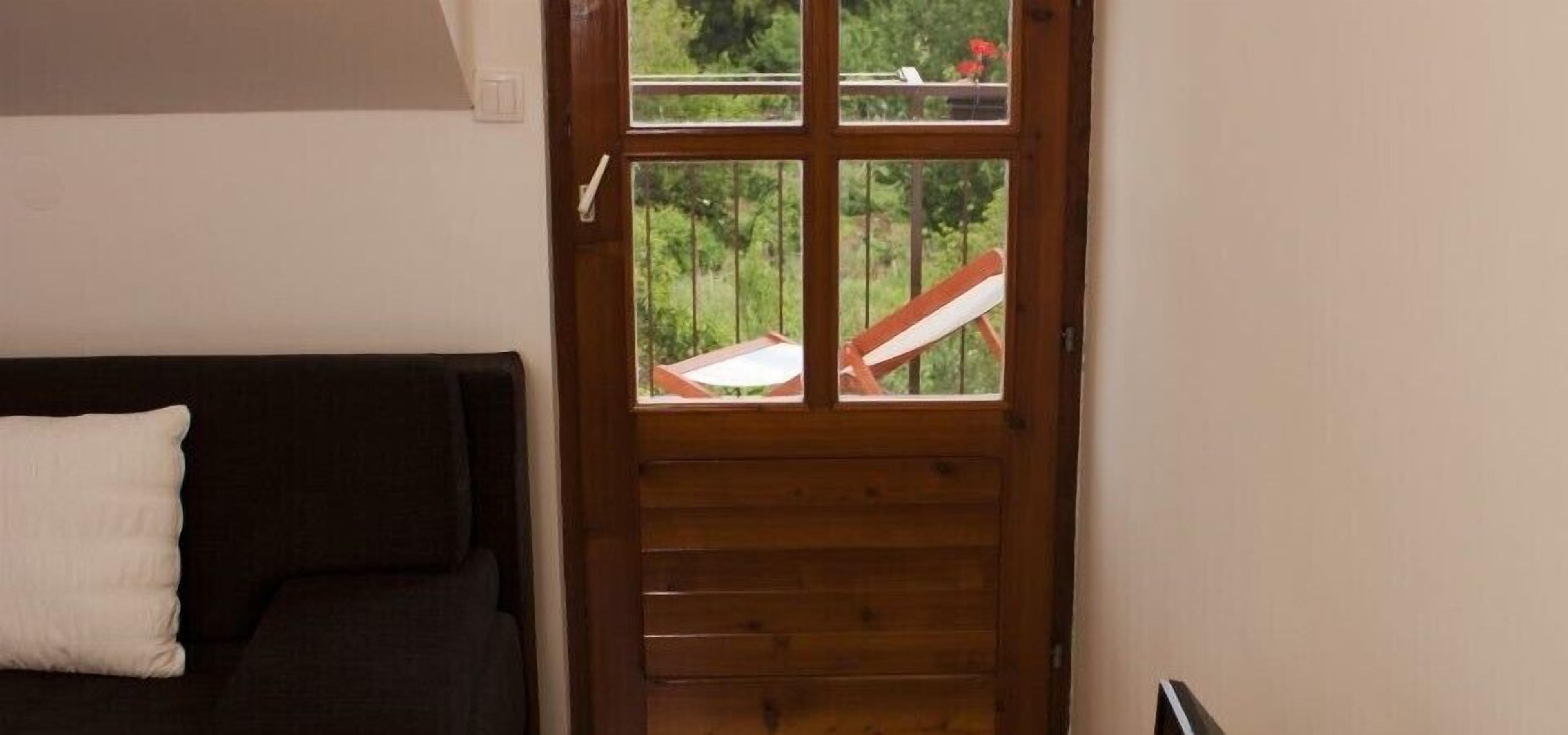 A wooden door with a view of a balcony with a chair.