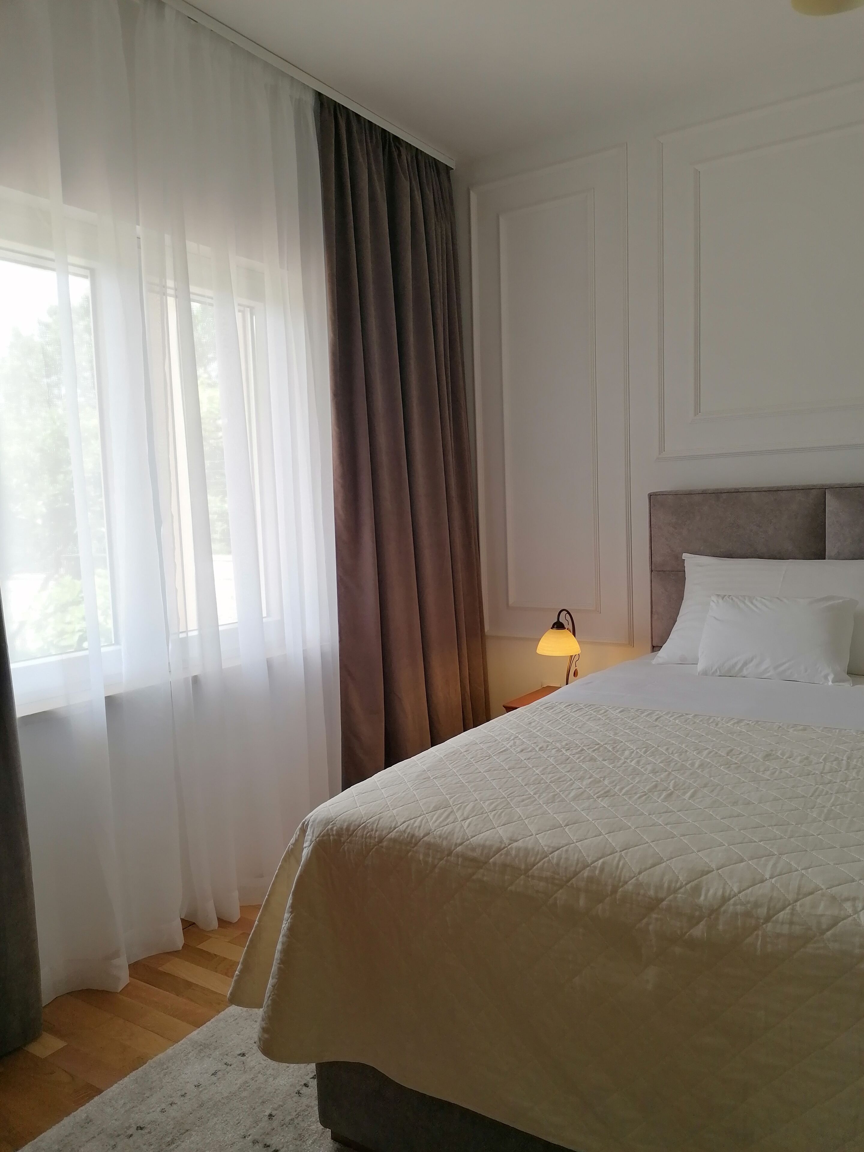 Ein Schlafzimmer mit einem Bett, einem Nachttisch, einer Lampe und einem Fenster mit Vorhängen.