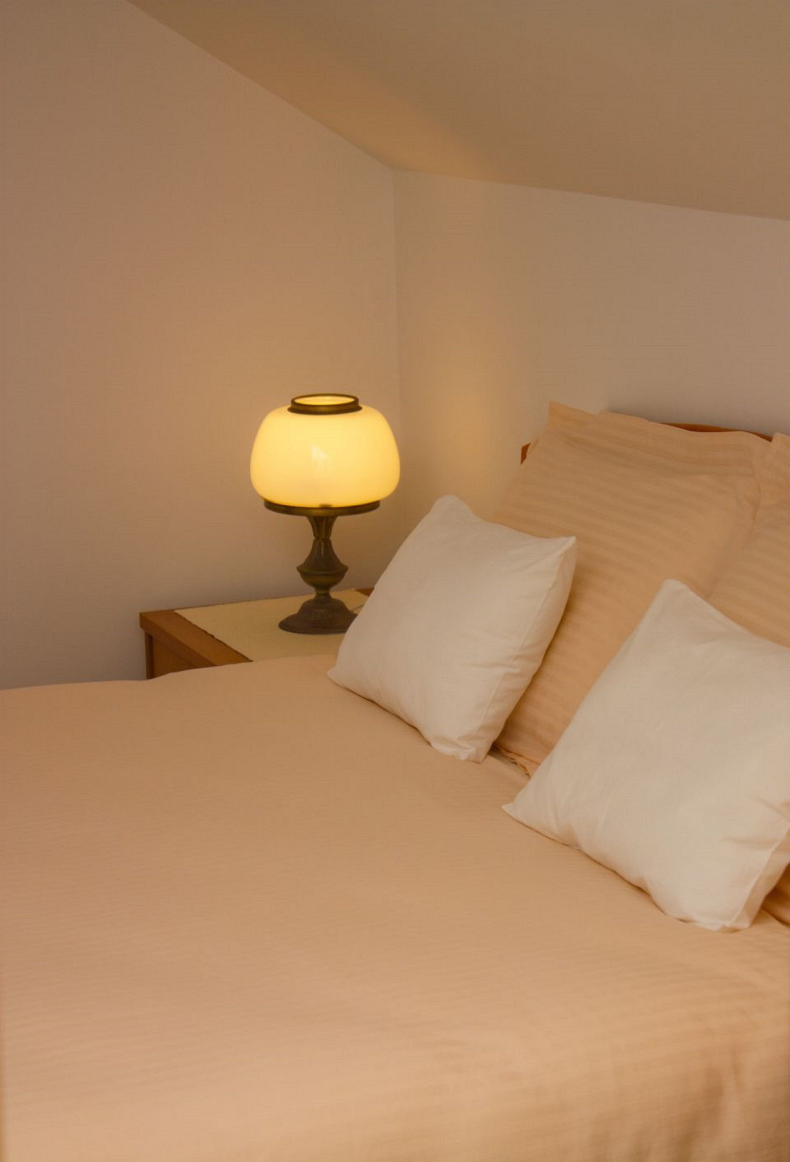 A neatly made bed with a beige comforter and pillows, a bedside lamp, and a wooden nightstand.