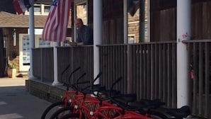 A row of red bicycles parked outside a building with an American flag. - Clegg's Hotel (Ocean Beach)