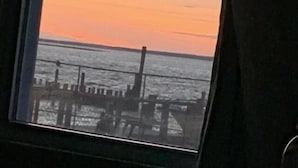 A window with a view of a sunset over the water, a dock, and a cloudy sky. - Clegg's Hotel (Ocean Beach)