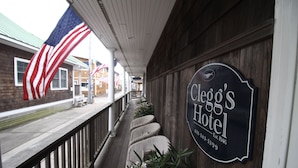 A wooden porch with wicker chairs and a sign for Cleo's Hotel. - Clegg's Hotel (Ocean Beach)