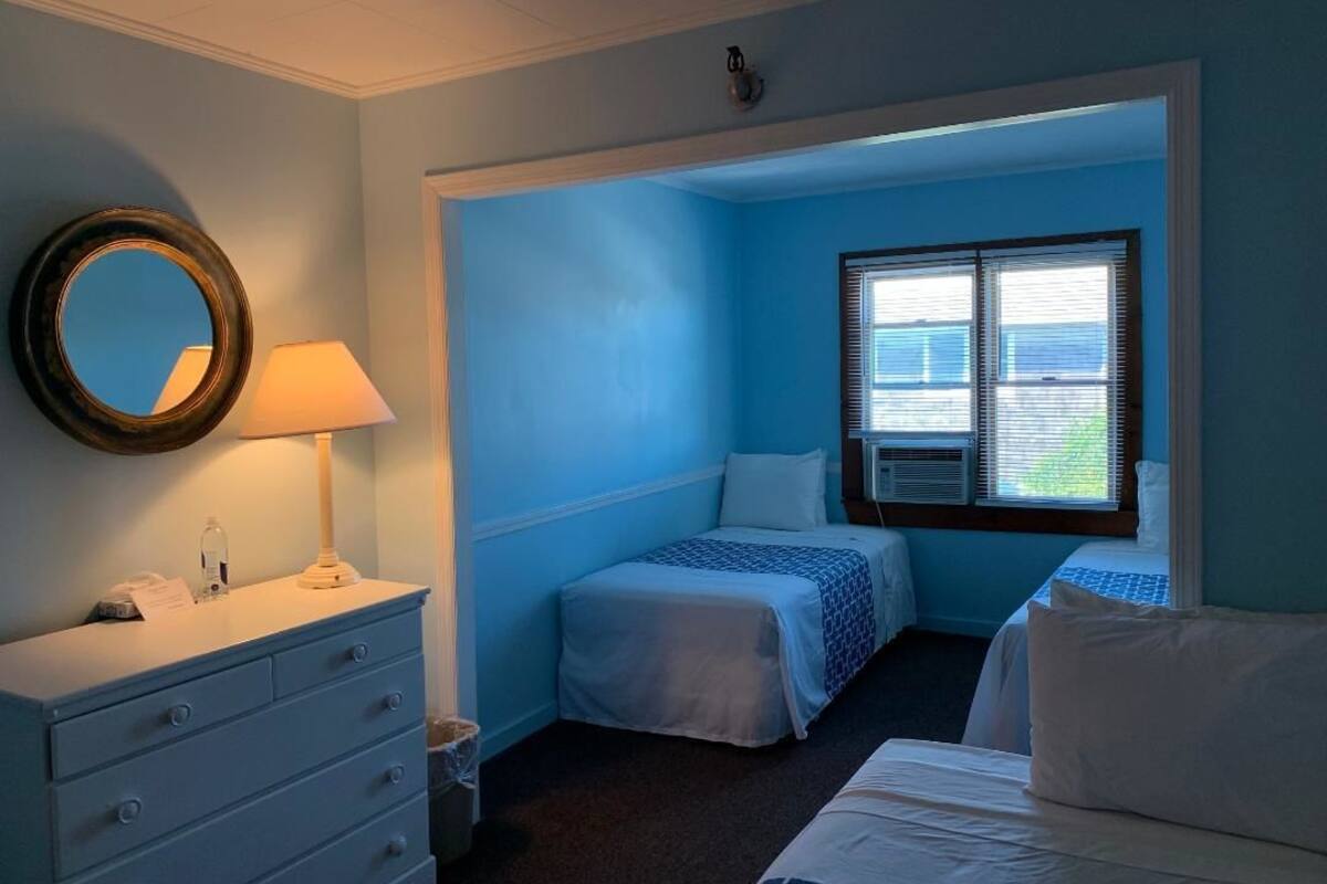 A room with two beds, a dresser, a mirror, and a window with blinds.