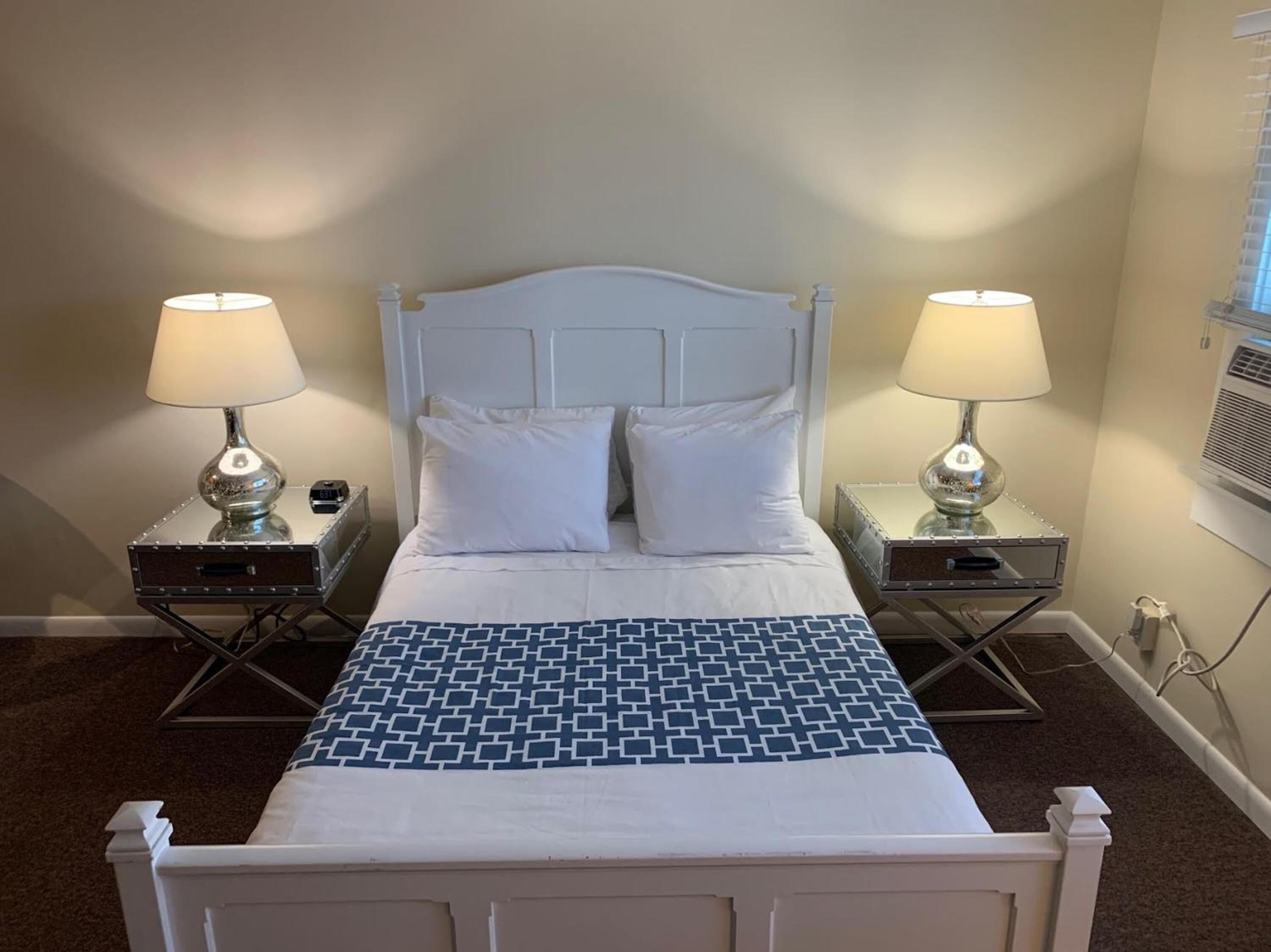 A neatly made bed with a white headboard, two bedside tables with lamps, and a patterned throw blanket.
