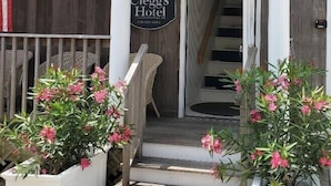 The entrance of Clegg's Hotel with a porch, steps, and potted plants. - Clegg's Hotel (Ocean Beach)